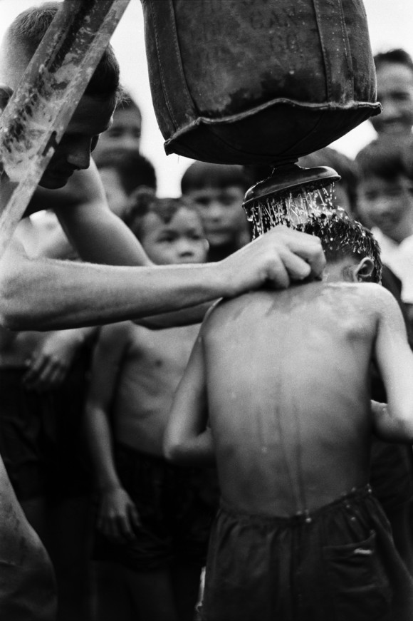 Um médico dá a um grupo de crianças vietnamitas um chuveiro com um saco de Lyster. Nomes, data e local desconhecidos.