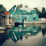 Artista pinta mural de ponta cabeça para ser visto no reflexo da água