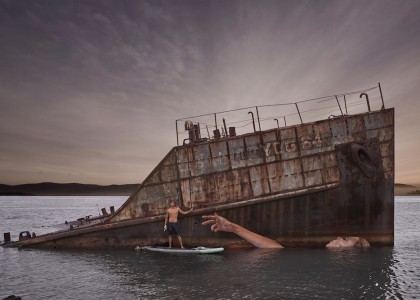 Sobre uma prancha, artista faz grafite em barco naufragado
